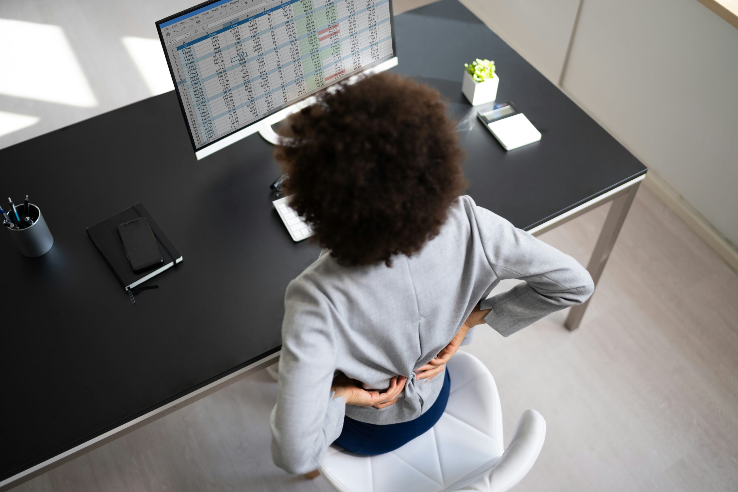 An office worker experiencing lower back pain while sitting at a desk, highlighting the need for better posture habits.